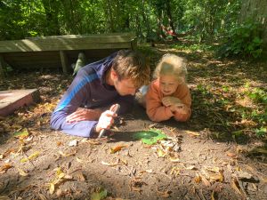 Forest School leader demonstrating how to burn letters into a leaf using a magnifying glass to an engaged child